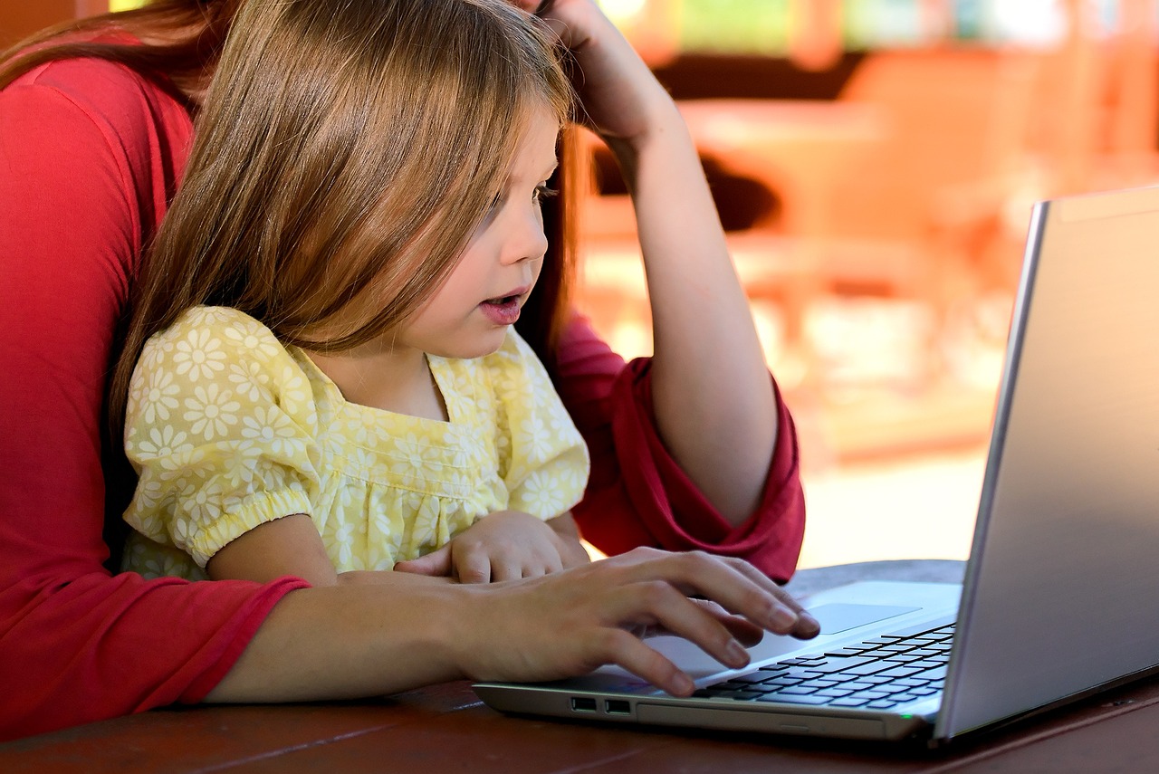 Image of girl sitting in caregiver lap looking at computer screen
