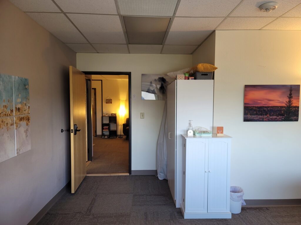 Exiting Playful Connection Counseling office to return to lobby. See a short white cabinet facing room, a taller white cabinet behind, facing hallway entering room.
